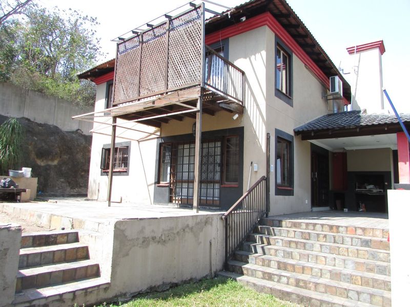 Rear view of a two-story house featuring a balcony, tiled patio area, built-in braai, and external staircase access.