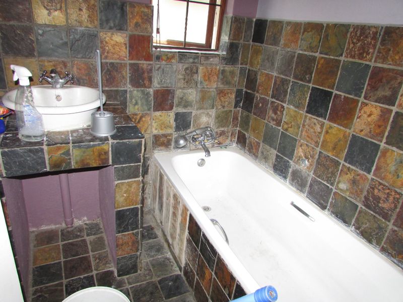 A dated bathroom featuring slate wall and floor tiles, a built-in vanity with a ceramic basin, and a standard bathtub.