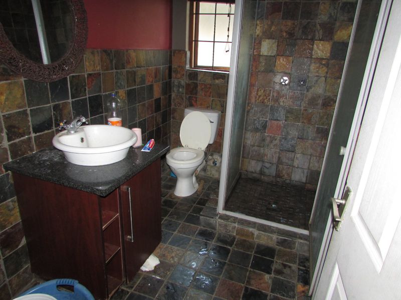 A dated bathroom featuring slate wall and floor tiles, a vessel sink on a granite vanity, and a separate shower enclosure.