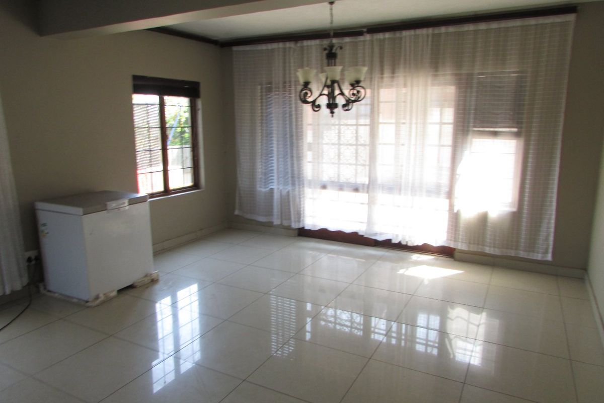 A spacious, empty living area featuring polished tiled flooring, a central chandelier, and large sliding glass doors providing natural light.