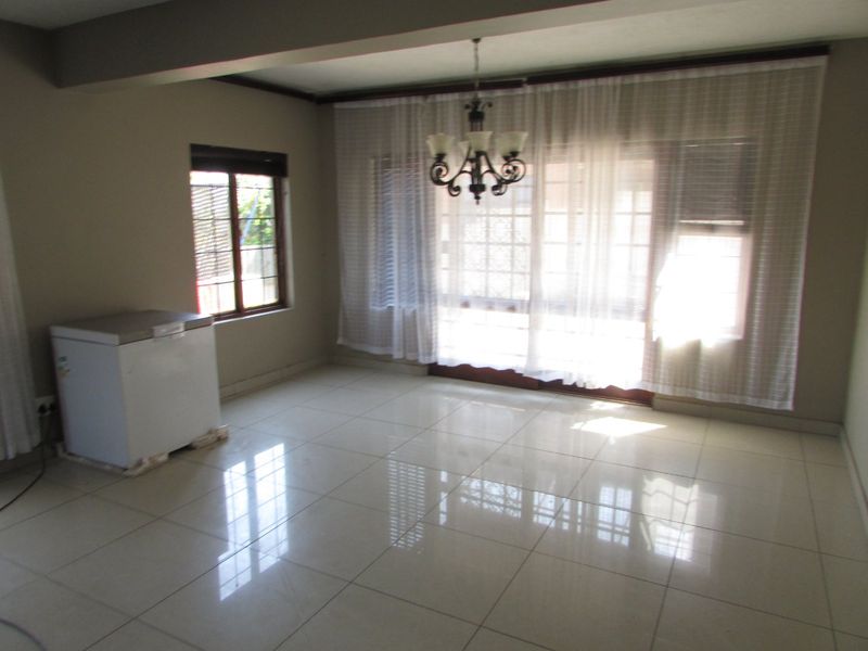 A spacious, empty living area featuring polished tiled flooring, a central chandelier, and large sliding glass doors providing natural light.