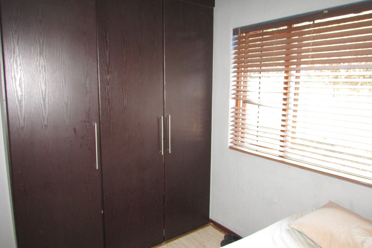A bedroom featuring dark wood built-in cupboards and window blinds, providing functional storage and light control.