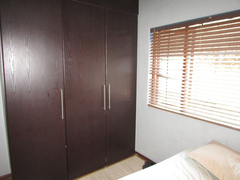 A bedroom featuring dark wood built-in cupboards and window blinds, providing functional storage and light control.