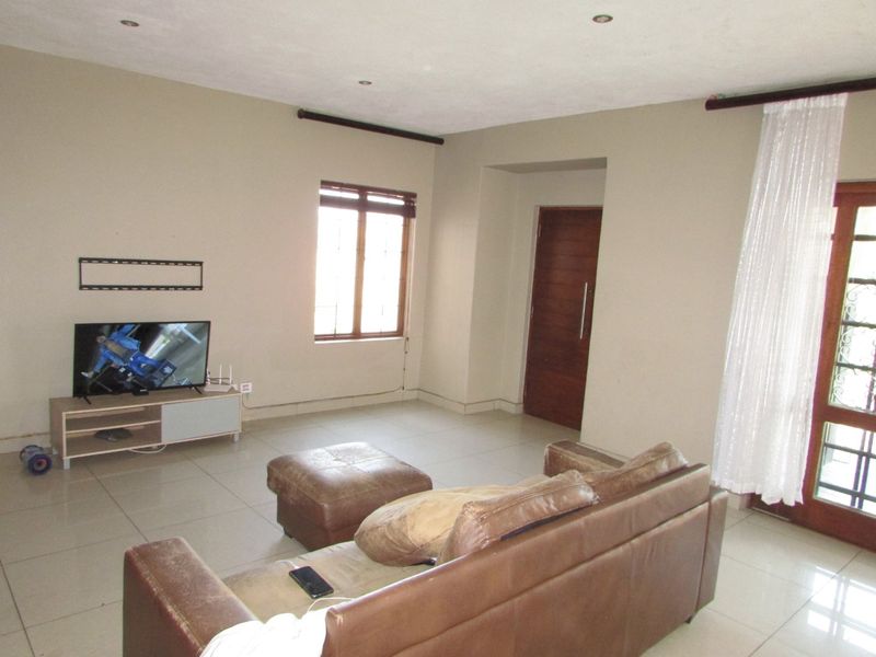 A living room featuring tiled flooring, recessed ceiling lighting, and access to an exterior door with natural light from a wooden-framed window.
