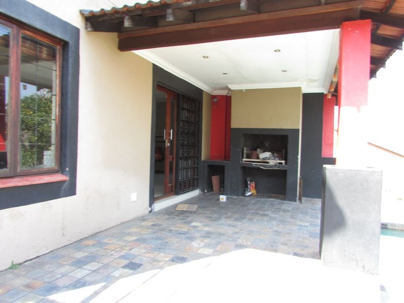 Covered patio area featuring a built-in braai, tiled flooring, and timber pergola structure, providing a functional outdoor entertainment space.
