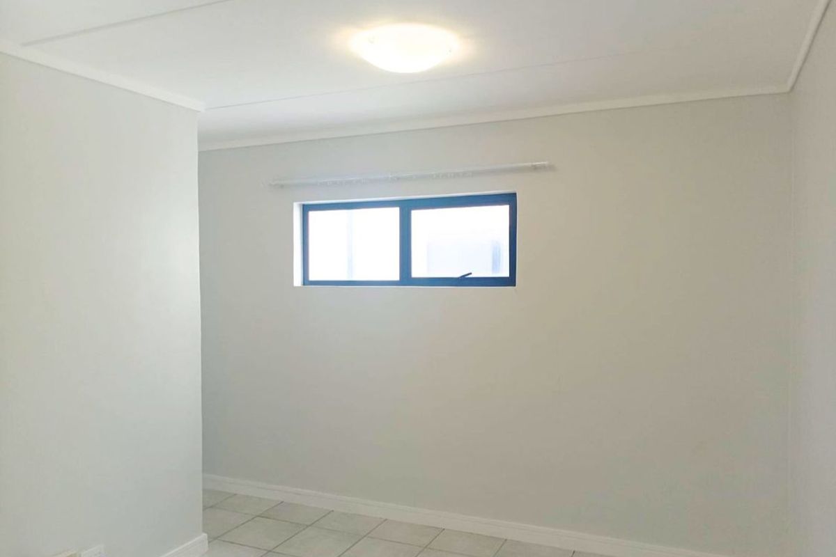 A clean, empty bedroom featuring neutral wall finishes, tiled flooring, and a functional aluminium window with an installed curtain rail.