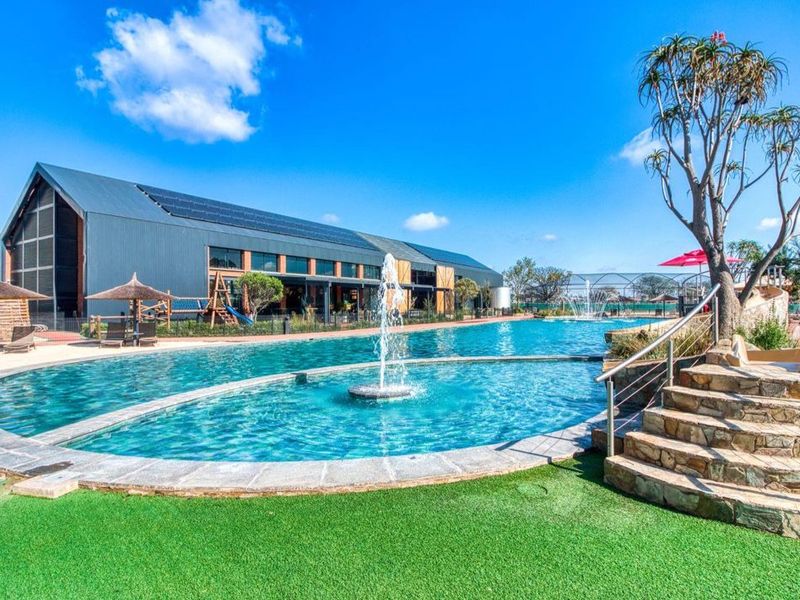 A well-maintained communal pool area featuring a central water fountain, stone steps, and modern building architecture with solar panels.
