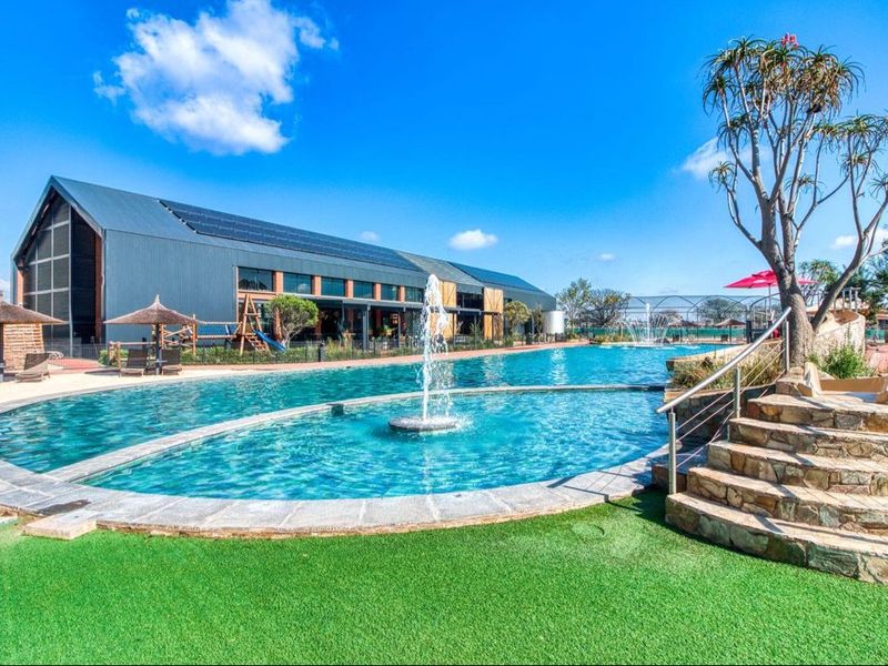 A well-maintained communal pool area featuring a central water fountain, stone steps with metal railings, and surrounding artificial turf landscaping.