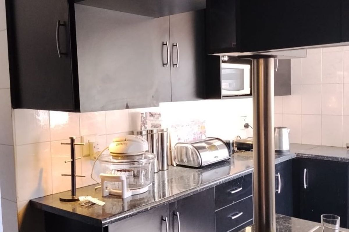 A functional kitchen featuring dark cabinetry, granite countertops, a tiled backsplash, and a built-in hob with a stainless steel support pillar.