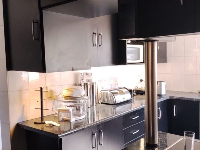 A functional kitchen featuring dark cabinetry, granite countertops, a tiled backsplash, and a built-in hob with a stainless steel support pillar.