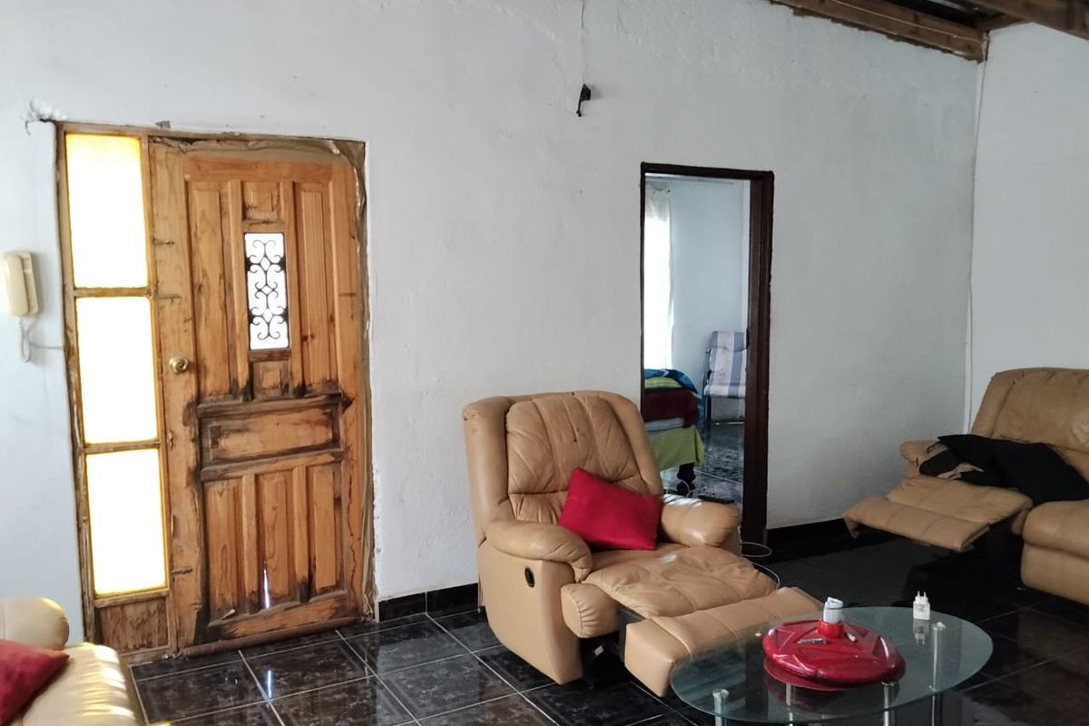 Living room featuring dark tiled flooring, exposed ceiling beams, and a timber entrance door with side light panel.