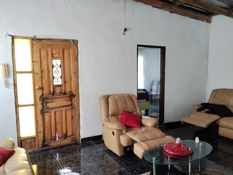 Living room featuring dark tiled flooring, exposed ceiling beams, and a timber entrance door with side light panel.