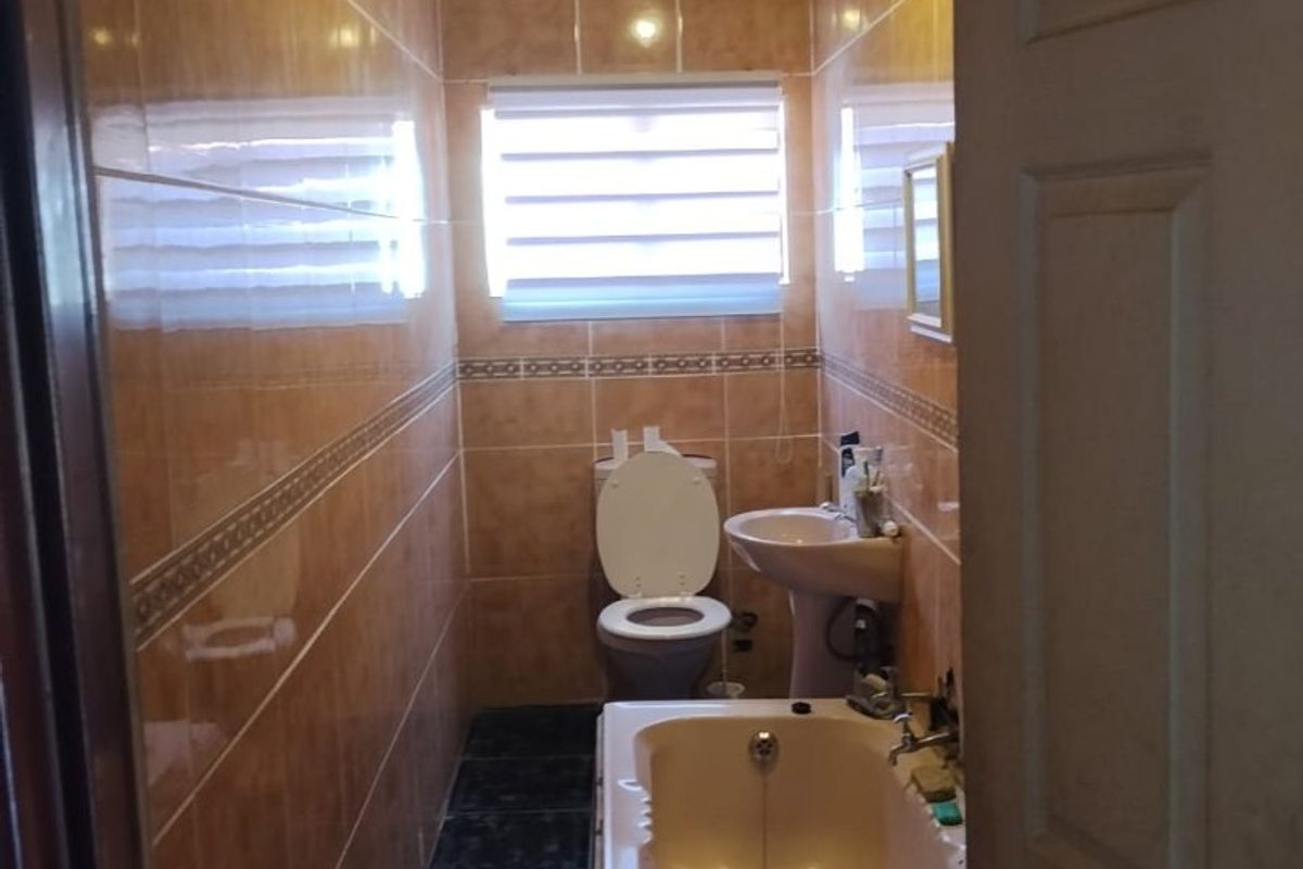 A compact bathroom featuring a pedestal basin, toilet, and bathtub with full-height wall tiling and an exposed roof structure.