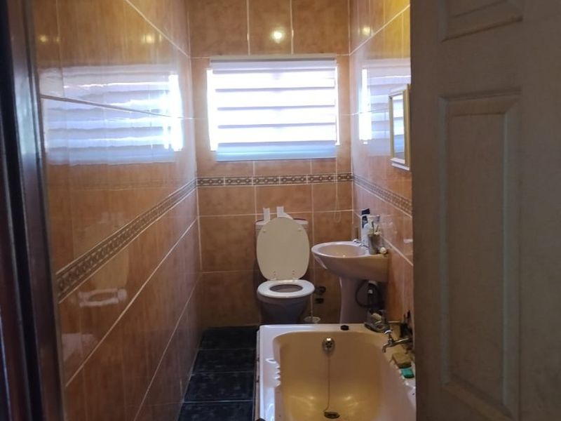 A compact bathroom featuring a pedestal basin, toilet, and bathtub with full-height wall tiling and an exposed roof structure.