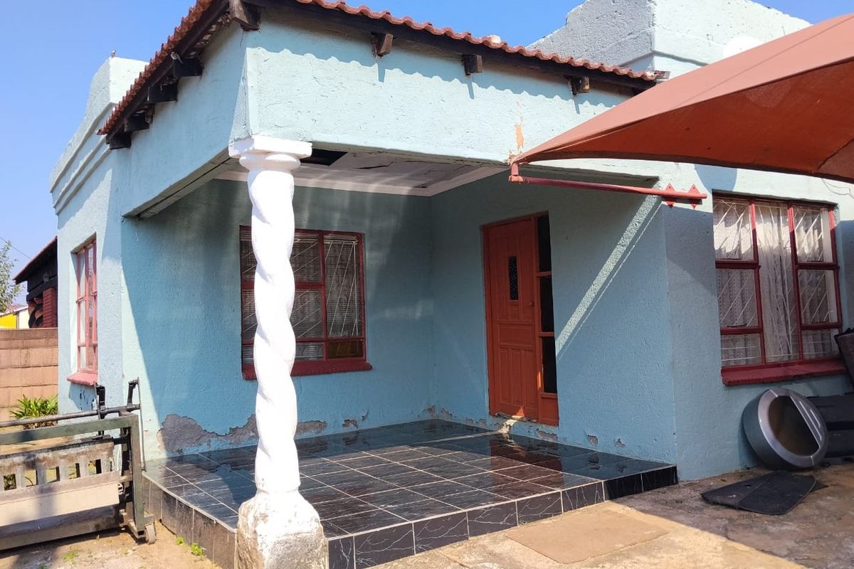 Front elevation of a house featuring a tiled patio, decorative column, and terracotta roof tiles, showing signs of exterior wear and maintenance requirements.