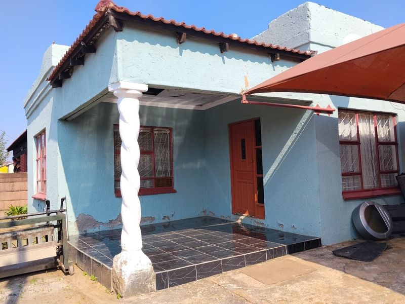 Front elevation of a house featuring a tiled patio, decorative column, and terracotta roof tiles, showing signs of exterior wear and maintenance requirements.