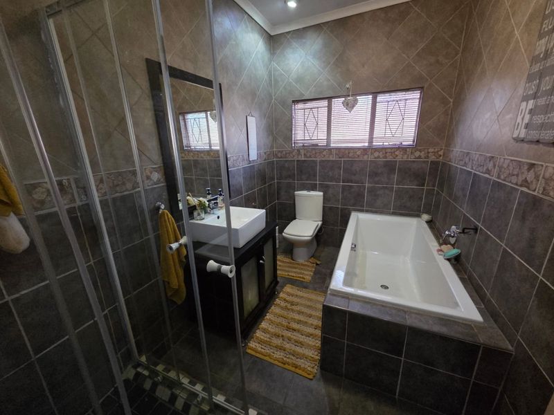 A functional bathroom featuring a built-in vanity with a vessel sink, a separate bathtub, and a glass-enclosed shower with full-height wall tiling.