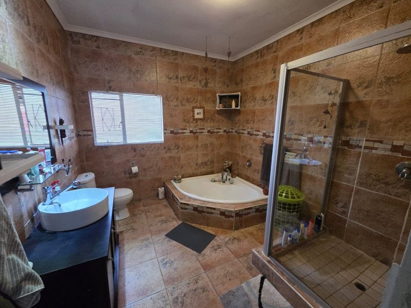 A functional bathroom featuring a corner bathtub, separate glass shower enclosure, vessel sink vanity, and full-height wall tiling.