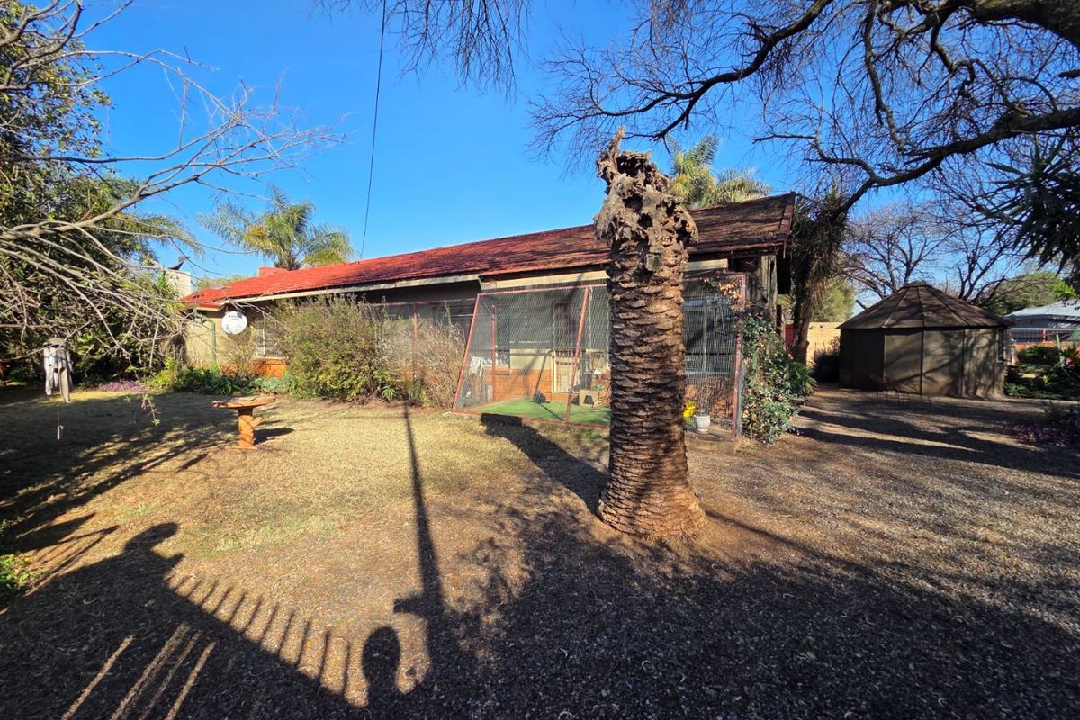 Rear view of the property featuring a corrugated metal roof, brick exterior, and an enclosed patio area set within a large garden space.