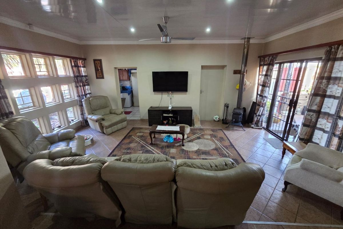 Spacious living room featuring tiled flooring, a wood-burning stove, ceiling fan, and large windows providing natural light with access to the outdoor area.