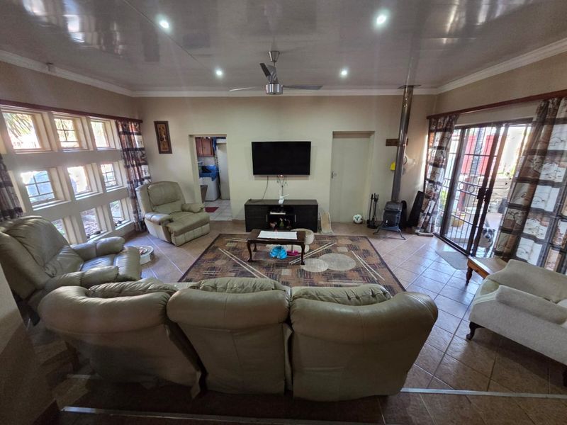 Spacious living room featuring tiled flooring, a wood-burning stove, ceiling fan, and large windows providing natural light with access to the outdoor area.