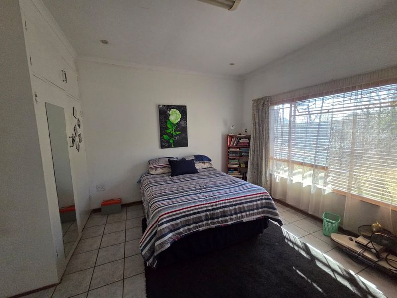 A functional bedroom featuring built-in cupboards, tiled flooring, and a large window that allows for ample natural light.