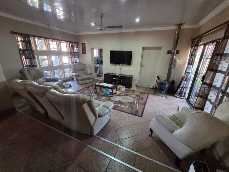 Spacious living room featuring tiled flooring, a wood-burning stove, ceiling fan, and large windows allowing for natural light.