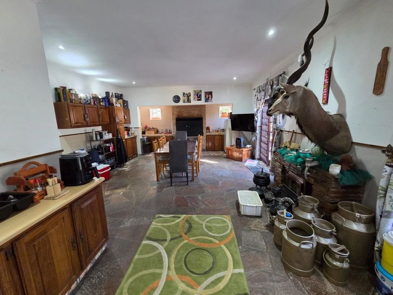 Spacious open-plan living and dining area featuring rustic stone flooring, built-in wooden cabinetry, and a brick fireplace, offering a versatile layout for family living.