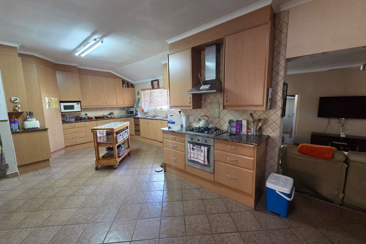 Spacious kitchen featuring light wood cabinetry, granite countertops, gas hob, and integrated oven, with tiled flooring and an open-plan layout.
