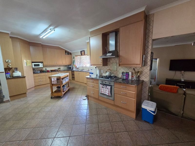 Spacious kitchen featuring light wood cabinetry, granite countertops, gas hob, and integrated oven, with tiled flooring and an open-plan layout.