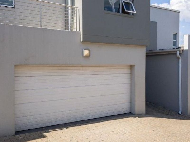 Modern townhouse exterior featuring double garage doors, a paved driveway, and an upper-level balcony with metal railings.