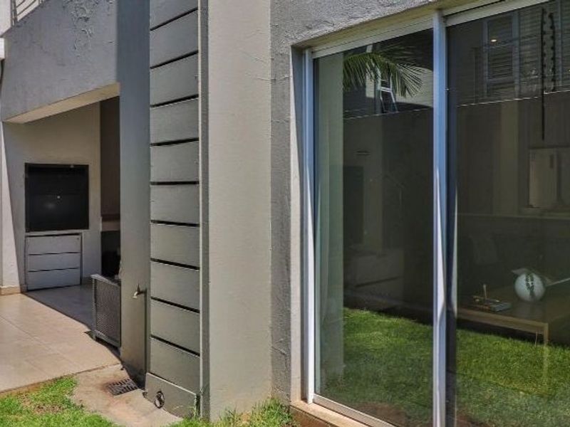 A covered patio area featuring a built-in braai, tiled flooring, and direct access to the interior through large sliding glass doors.