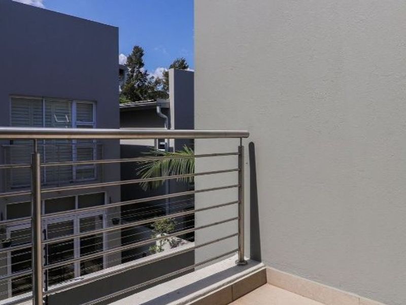 A modern balcony featuring a stainless steel balustrade and tiled flooring, overlooking the surrounding townhouse complex.