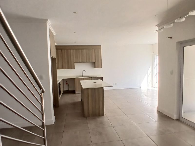 Spacious open-plan living and kitchen area featuring modern cabinetry, a central island, tiled flooring, and a staircase with a contemporary metal balustrade.