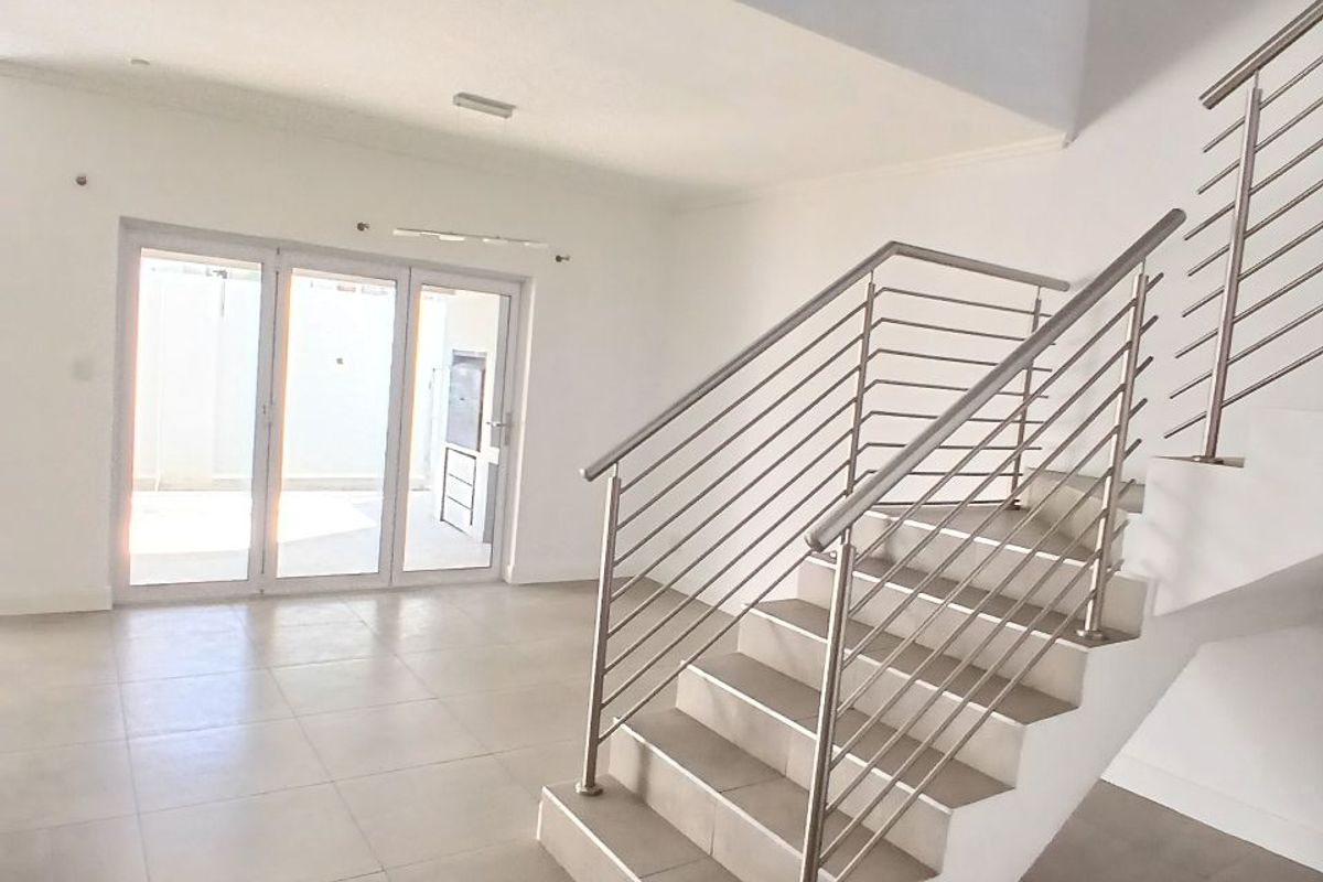 Bright and spacious open-plan living area featuring modern tiled flooring, a central staircase with stainless steel balustrades, and sliding doors leading to the exterior.