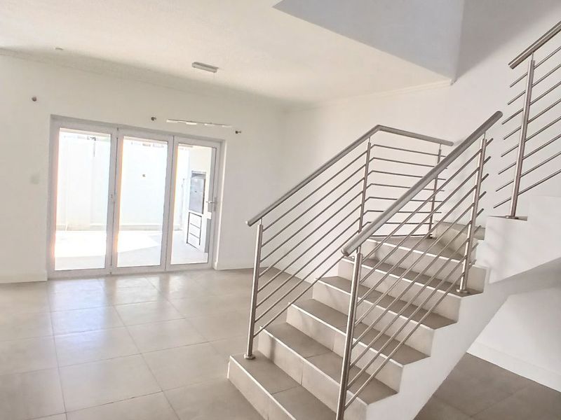 Bright and spacious open-plan living area featuring modern tiled flooring, a central staircase with stainless steel balustrades, and sliding doors leading to the exterior.