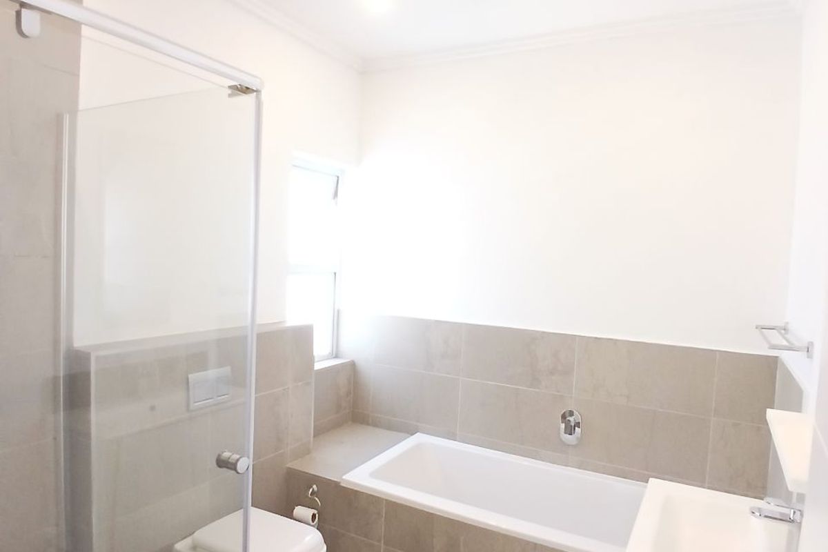 Modern bathroom featuring a glass-enclosed shower, wall-hung toilet, built-in bathtub, and vanity basin with neutral tiled finishes.