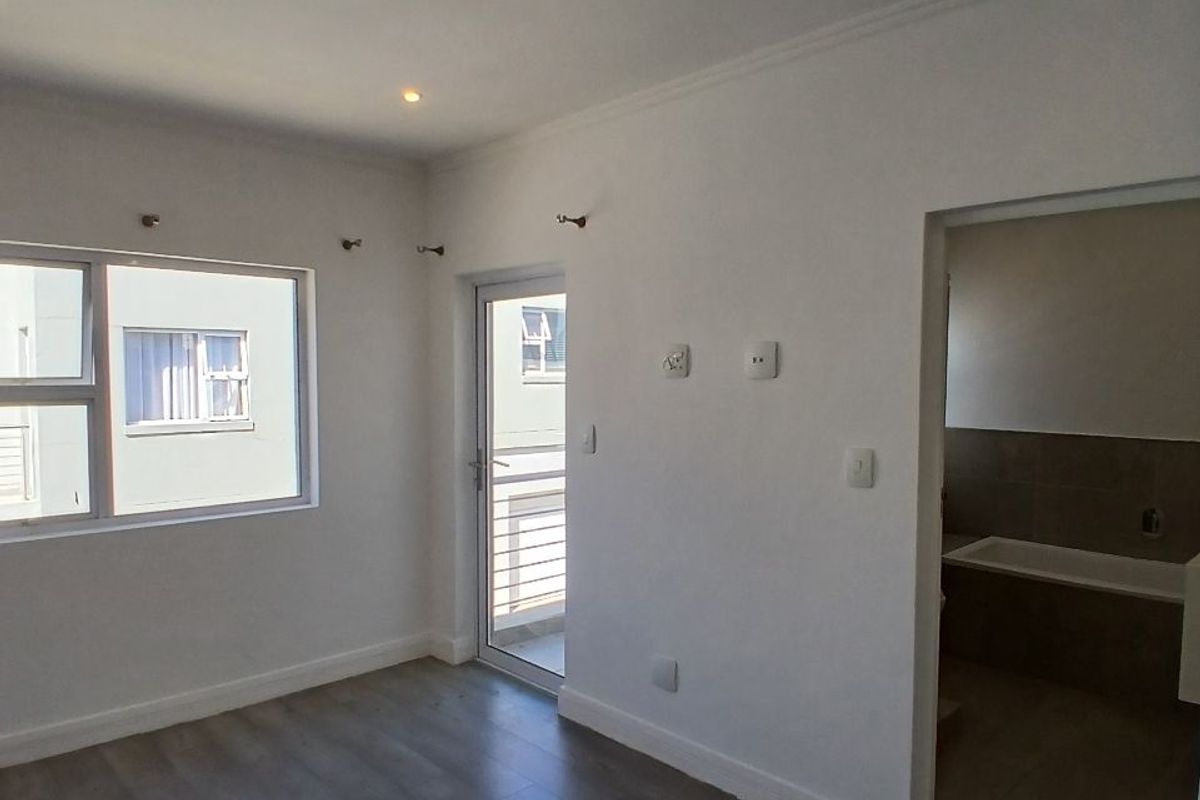 A bright, empty bedroom featuring modern laminate flooring, recessed downlighting, and direct access to an en-suite bathroom.