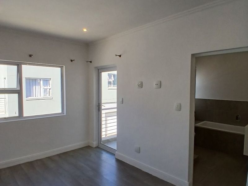 A bright, empty bedroom featuring modern laminate flooring, recessed downlighting, and direct access to an en-suite bathroom.