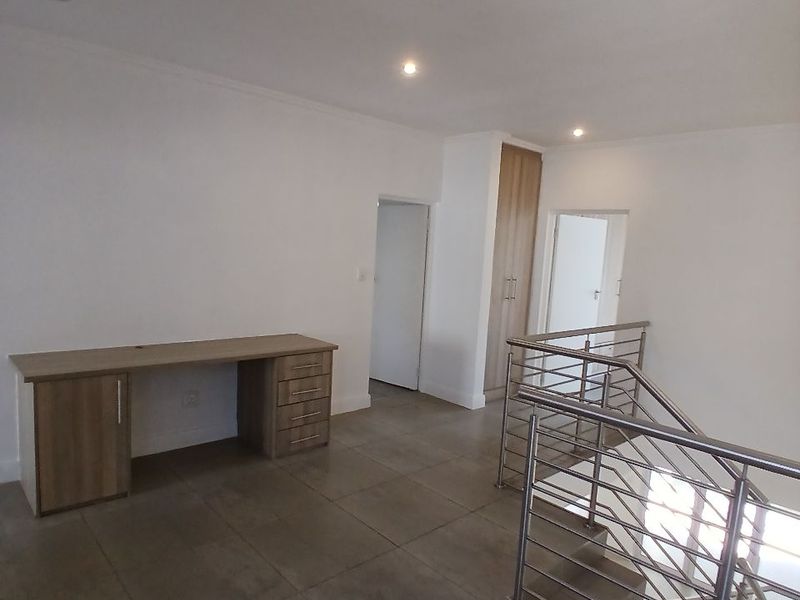 Spacious landing area featuring tiled flooring, a built-in desk, integrated storage cupboard, and a modern stainless steel staircase balustrade.