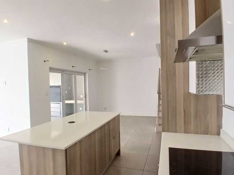 Modern open-plan kitchen and living area featuring a central island, sleek cabinetry, integrated hob, and neutral tiled flooring in a bright, spacious layout.