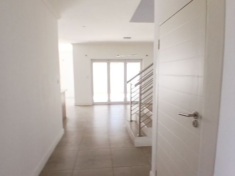 A bright, empty hallway featuring tiled flooring and a staircase with a modern stainless steel balustrade, leading towards an open-plan living area.