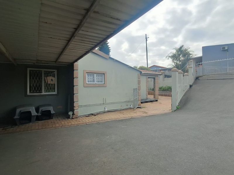 Exterior view of the property featuring a covered carport, paved driveway, and secure gated entrance with boundary walling.