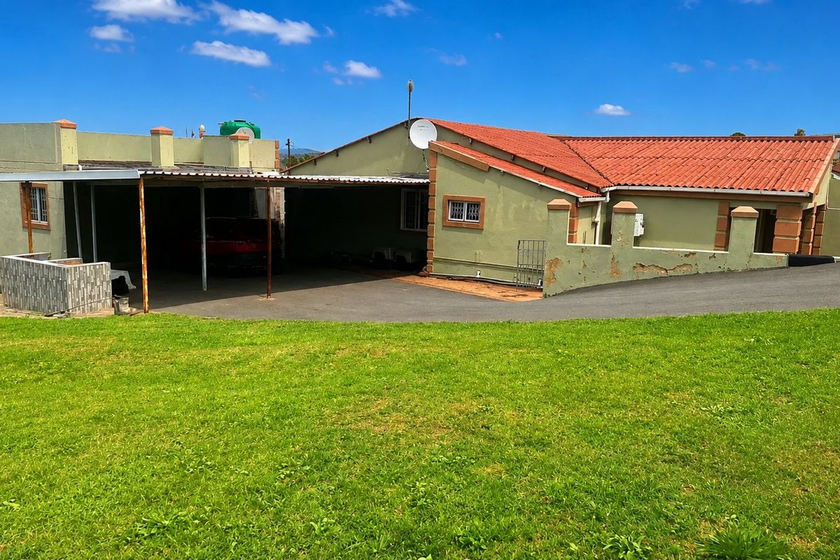 Rear view of the property featuring a large lawn, a covered carport area, and a tiled roof structure with visible exterior wall maintenance required.