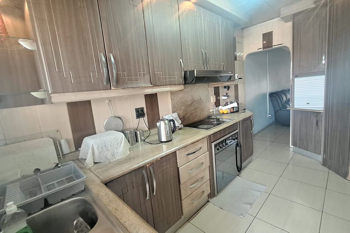 A functional kitchen featuring wood-grain cabinetry, laminate countertops, integrated oven and hob, and tiled flooring, offering a practical layout for daily meal preparation.