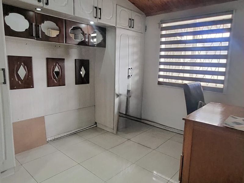 Bedroom featuring built-in cupboards, tiled flooring, and a timber ceiling. The room includes a window with roller blinds and requires minor maintenance.