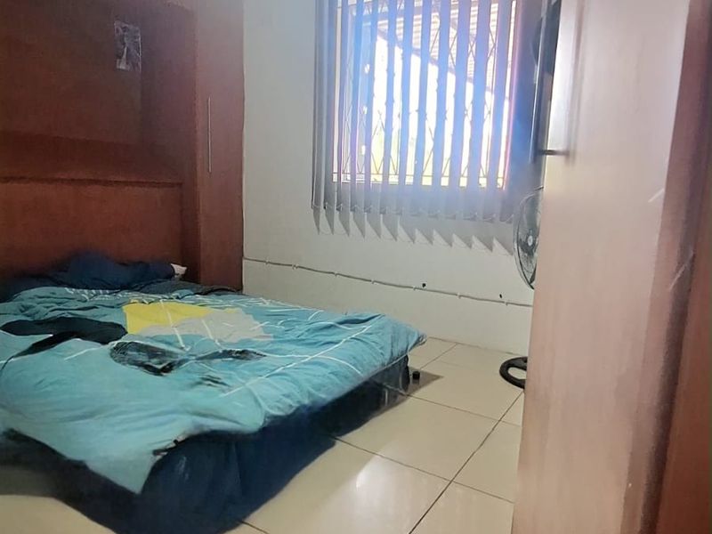A bedroom featuring built-in wooden cupboards, tiled flooring, and a timber ceiling, with vertical blinds and security bars on the window.