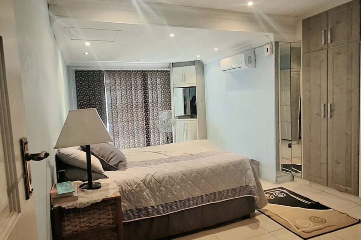 A functional bedroom featuring tiled flooring, built-in cupboards with mirrored accents, recessed lighting, and a wall-mounted air conditioning unit.