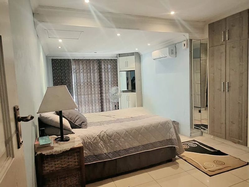A functional bedroom featuring tiled flooring, built-in cupboards with mirrored accents, recessed lighting, and a wall-mounted air conditioning unit.