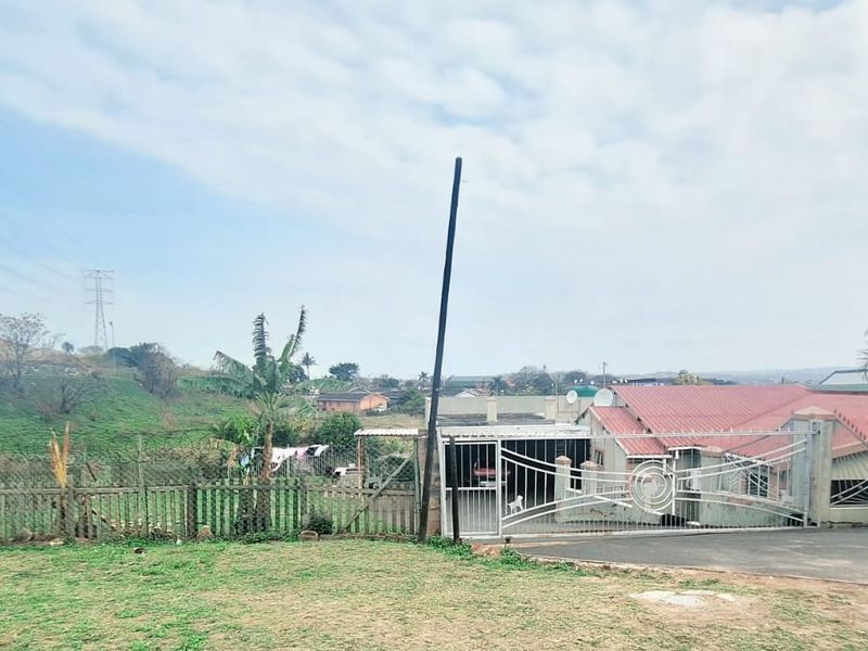 Front view of the property featuring a metal security gate, perimeter fencing, and a pitched metal roof, set within a suburban landscape.